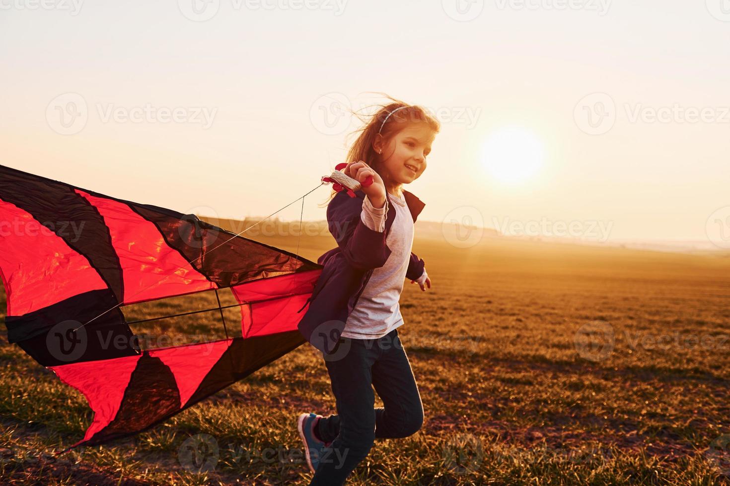 Happy little girl running with kite in hands on the beautiful field at sunrishe time photo