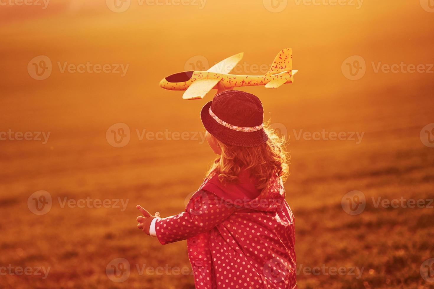 Illuminated by sunlight. Cute little girl have fun with toy plane on the beautiful field at daytime photo