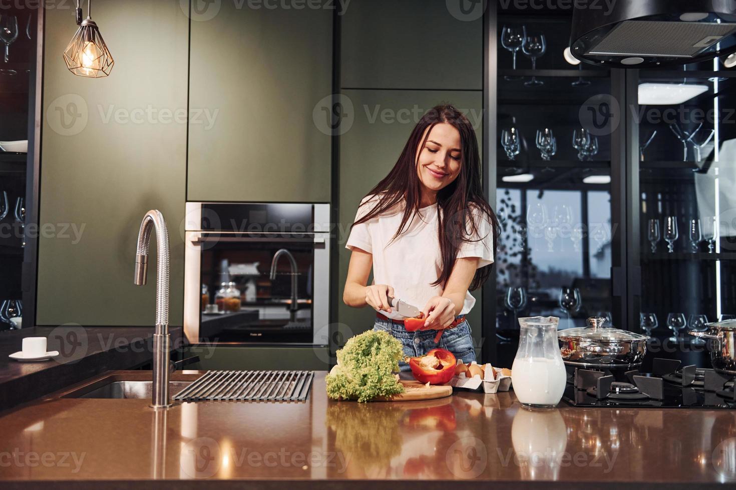 joven y hermosa morena con ropa informal preparando comida saludable en la cocina durante el día foto