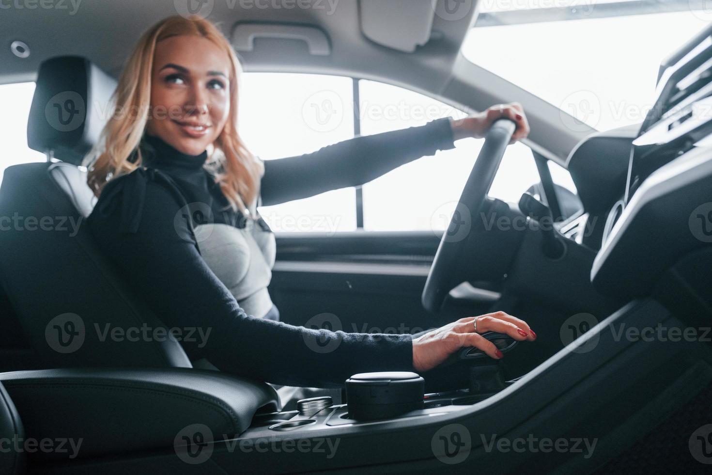 Side view of beautiful blonde in elegant clothes that sitting inside of modern car photo