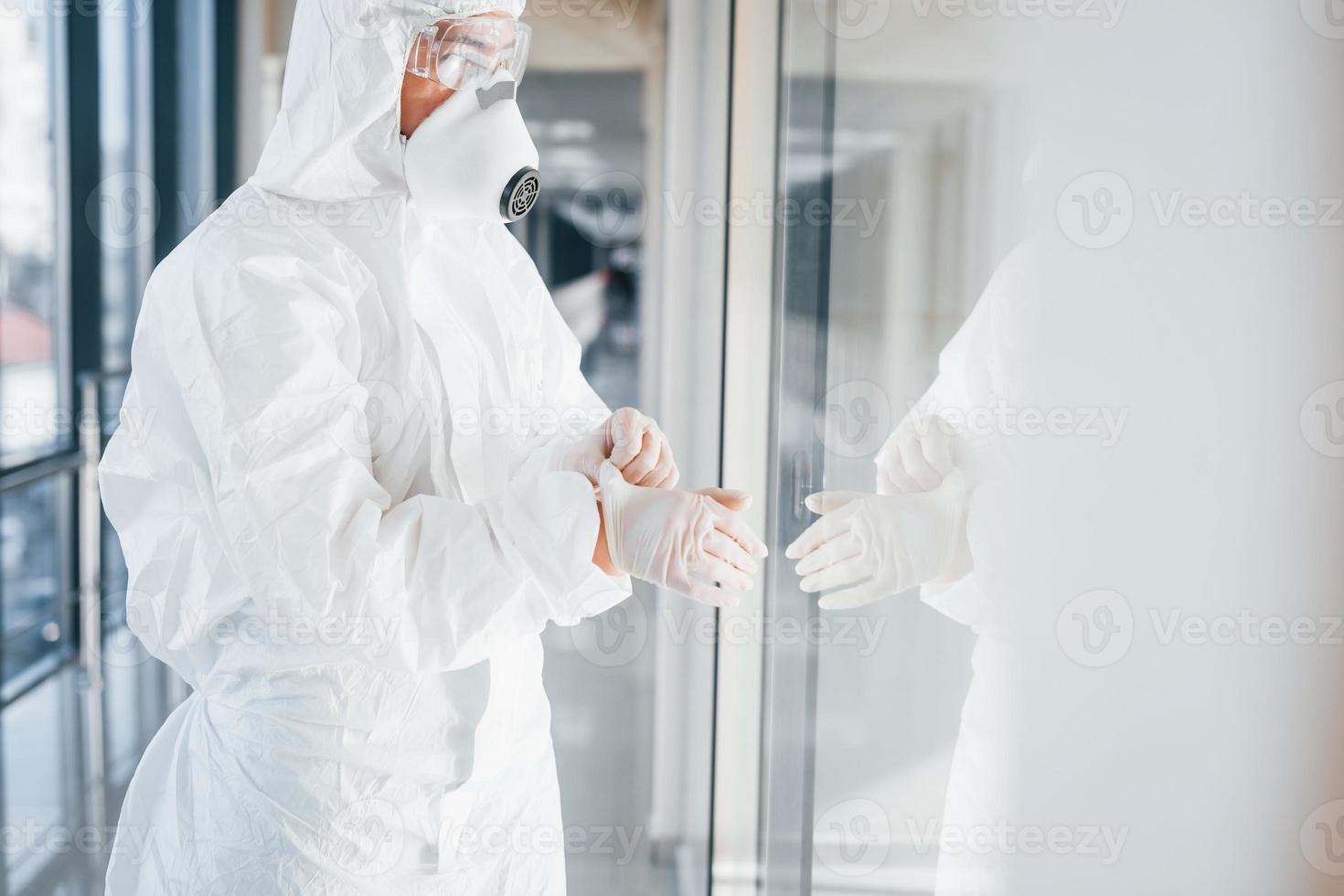 Female doctor scientist in lab coat, defensive eyewear and mask standing indoors and wearing gloves photo