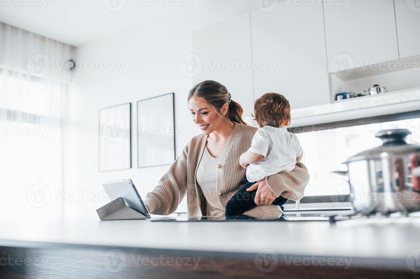 Female blogger mother with her kid together indoors at home at weekend using tablet photo