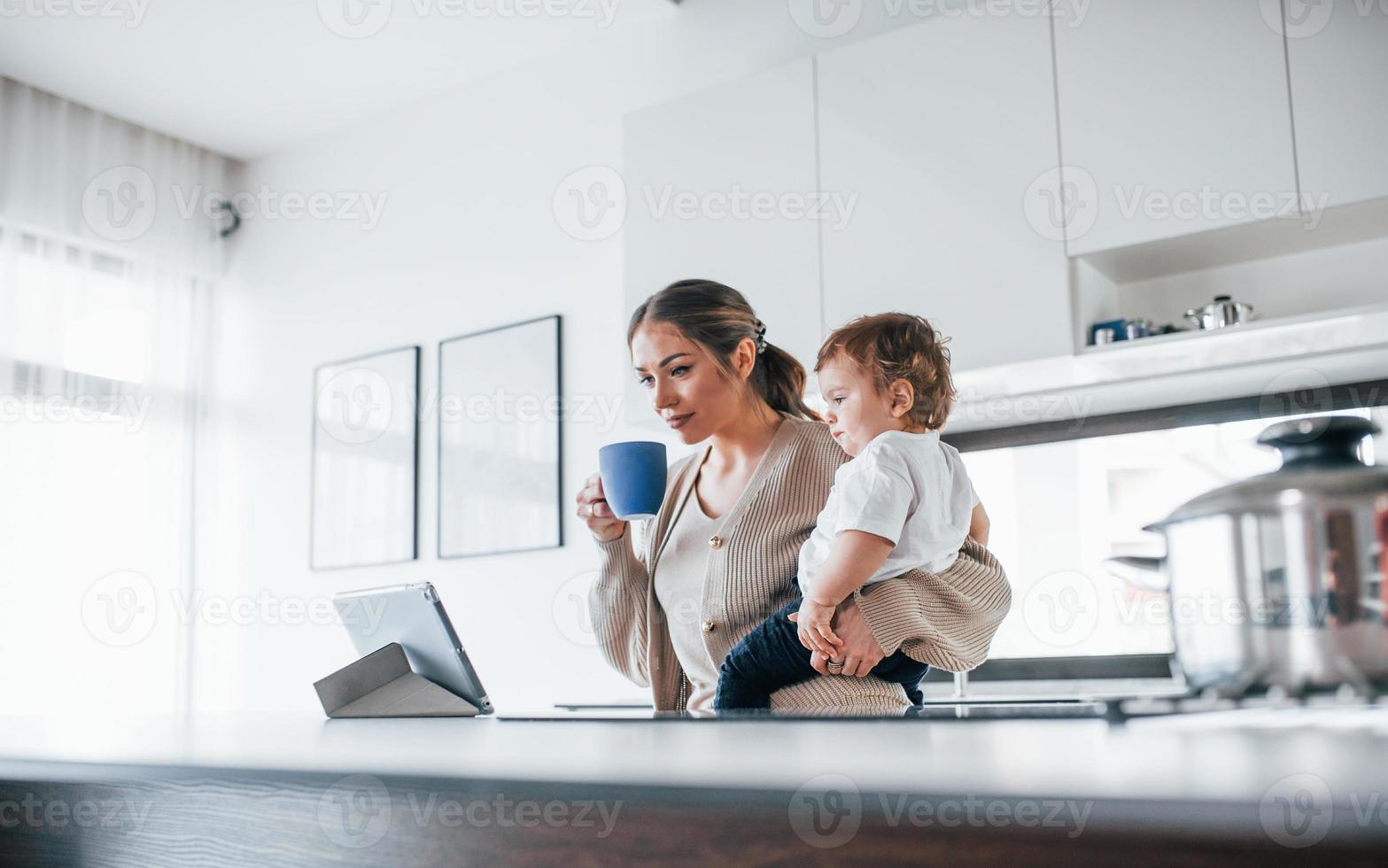 Female blogger mother with her kid together indoors at home at weekend using tablet photo