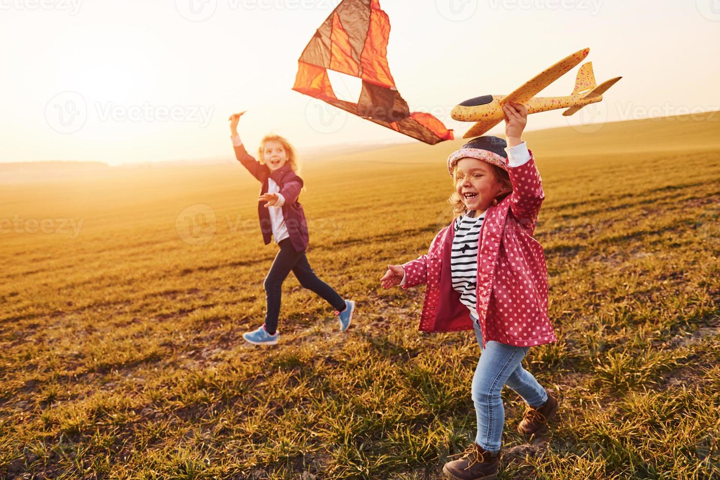 Two little girls friends have fun together with kite and toy plane on the field at sunny daytime photo