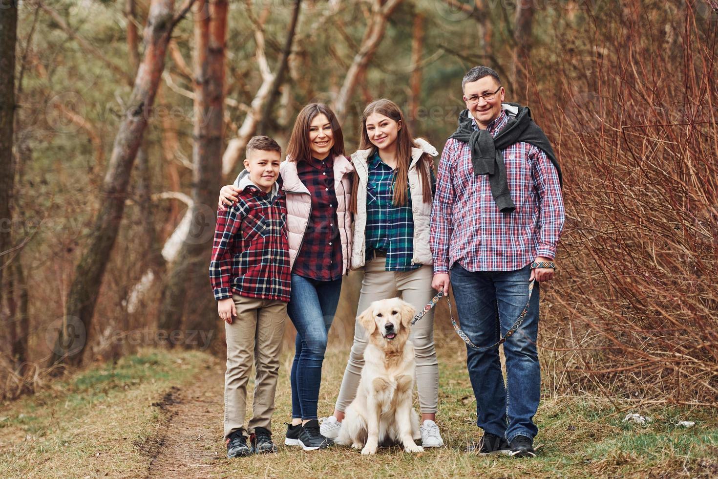Happy family standing together with their dog outdoors in forest photo