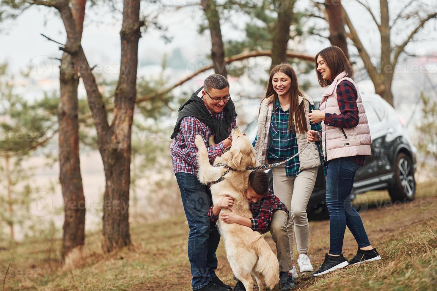 Happy family have fun with their active dog near modern car outdoors in forest photo