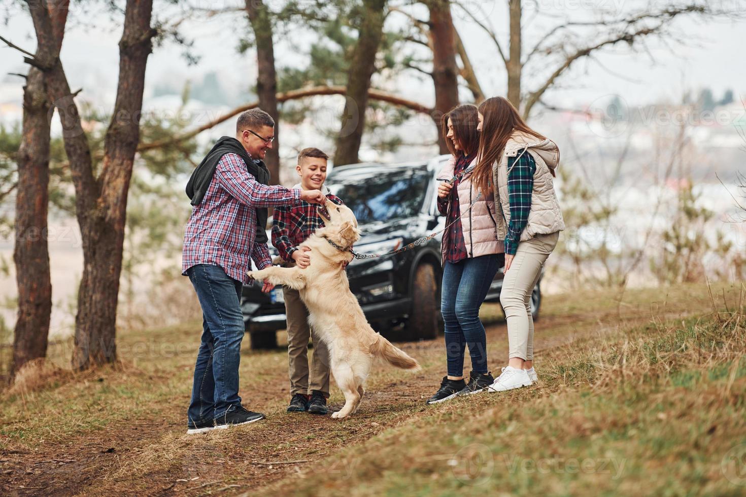 Happy family have fun with their active dog near modern car outdoors in forest photo