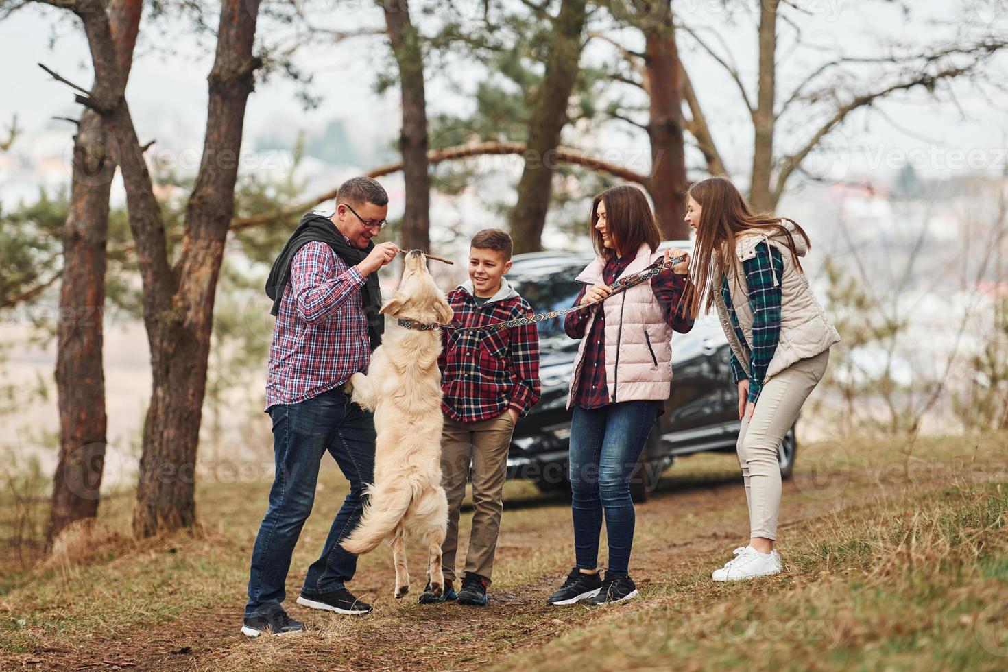 Happy family have fun with their active dog near modern car outdoors in forest photo