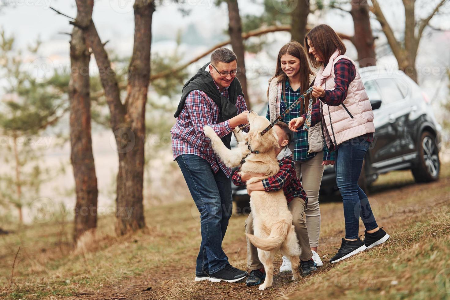 Happy family have fun with their active dog near modern car outdoors in forest photo