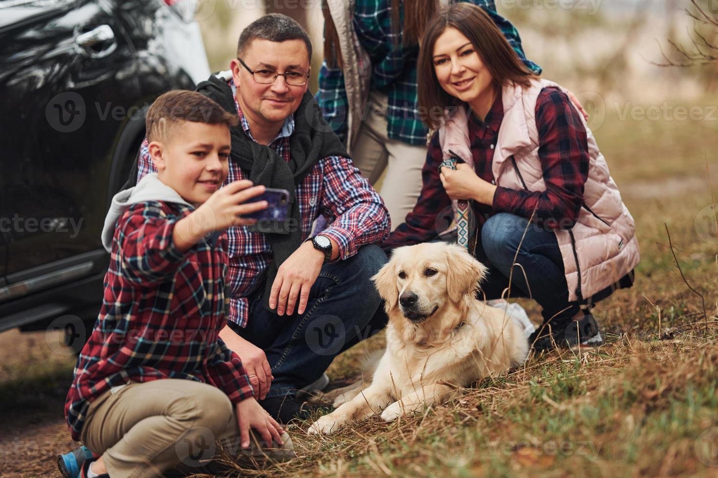 Happy family sitting and having fun with their dog near modern car outdoors in forest photo
