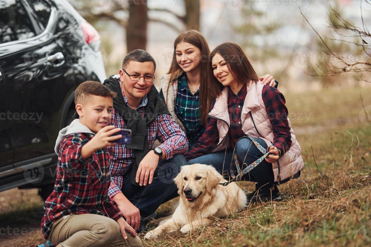 Happy family sitting and having fun with their dog near modern car outdoors in forest photo