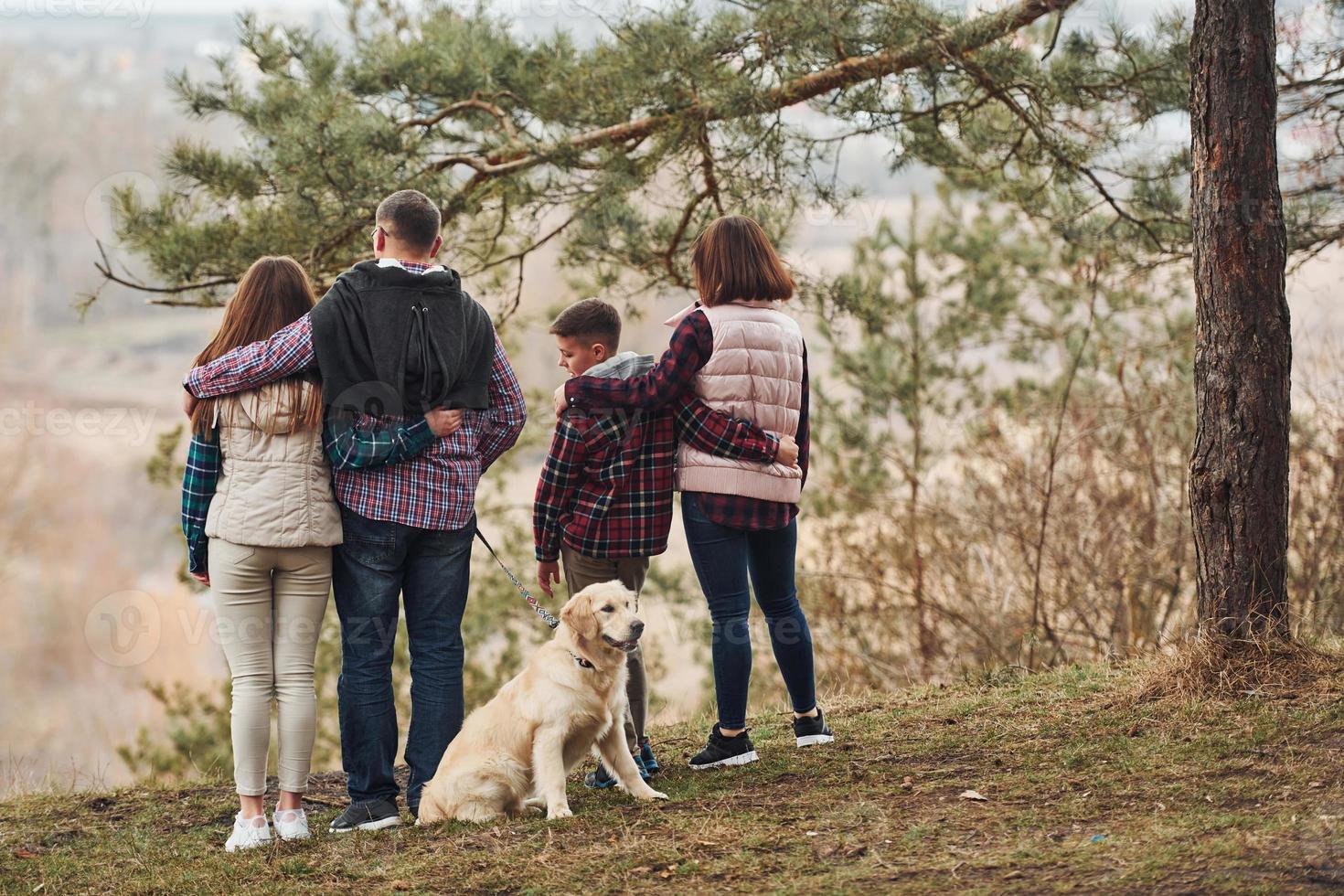 Rear view of family that standing together with their dog outdoors in forest photo