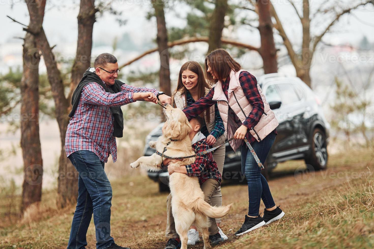 Happy family have fun with their active dog near modern car outdoors in forest photo