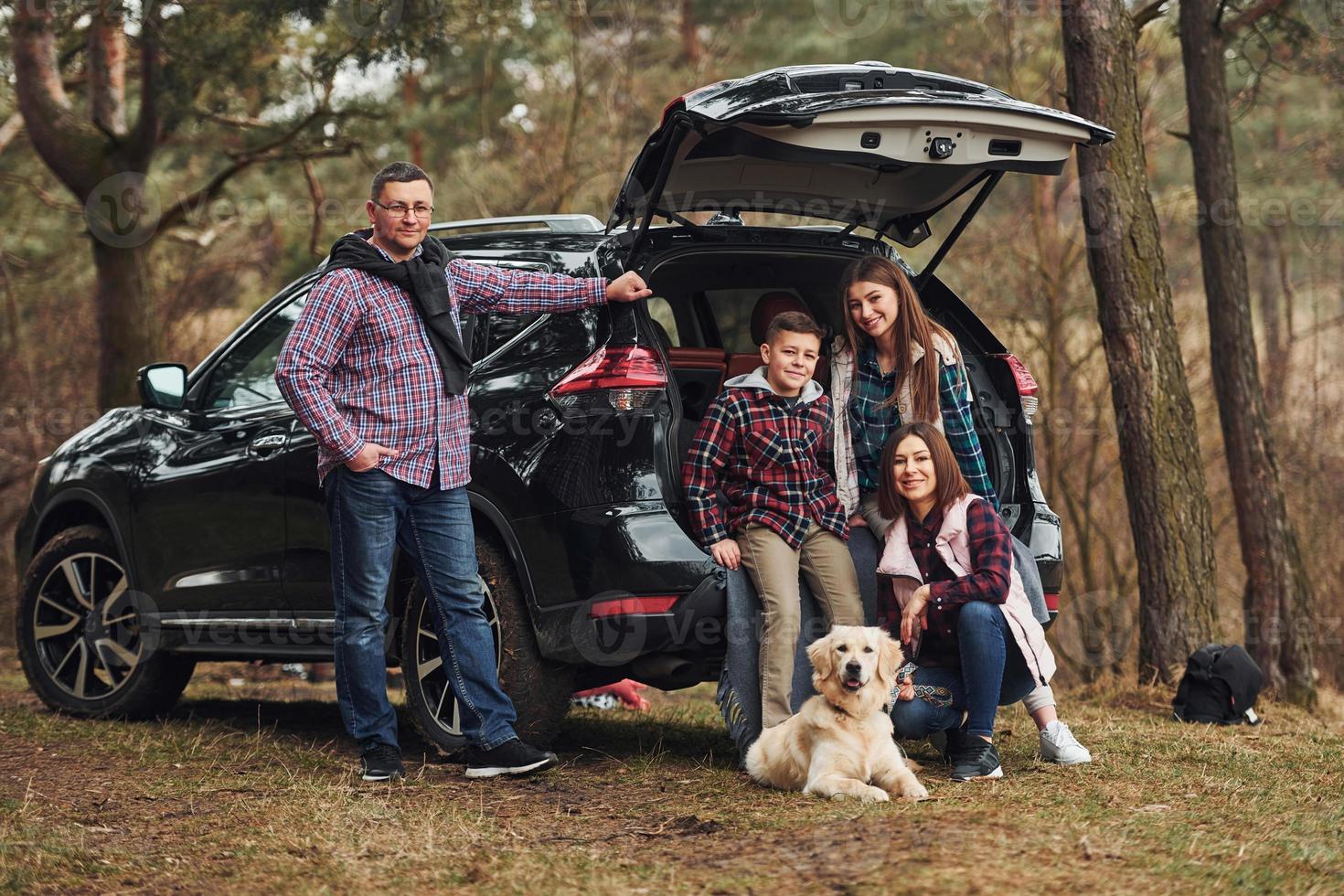 Happy family have fun with their dog near modern car outdoors in forest photo