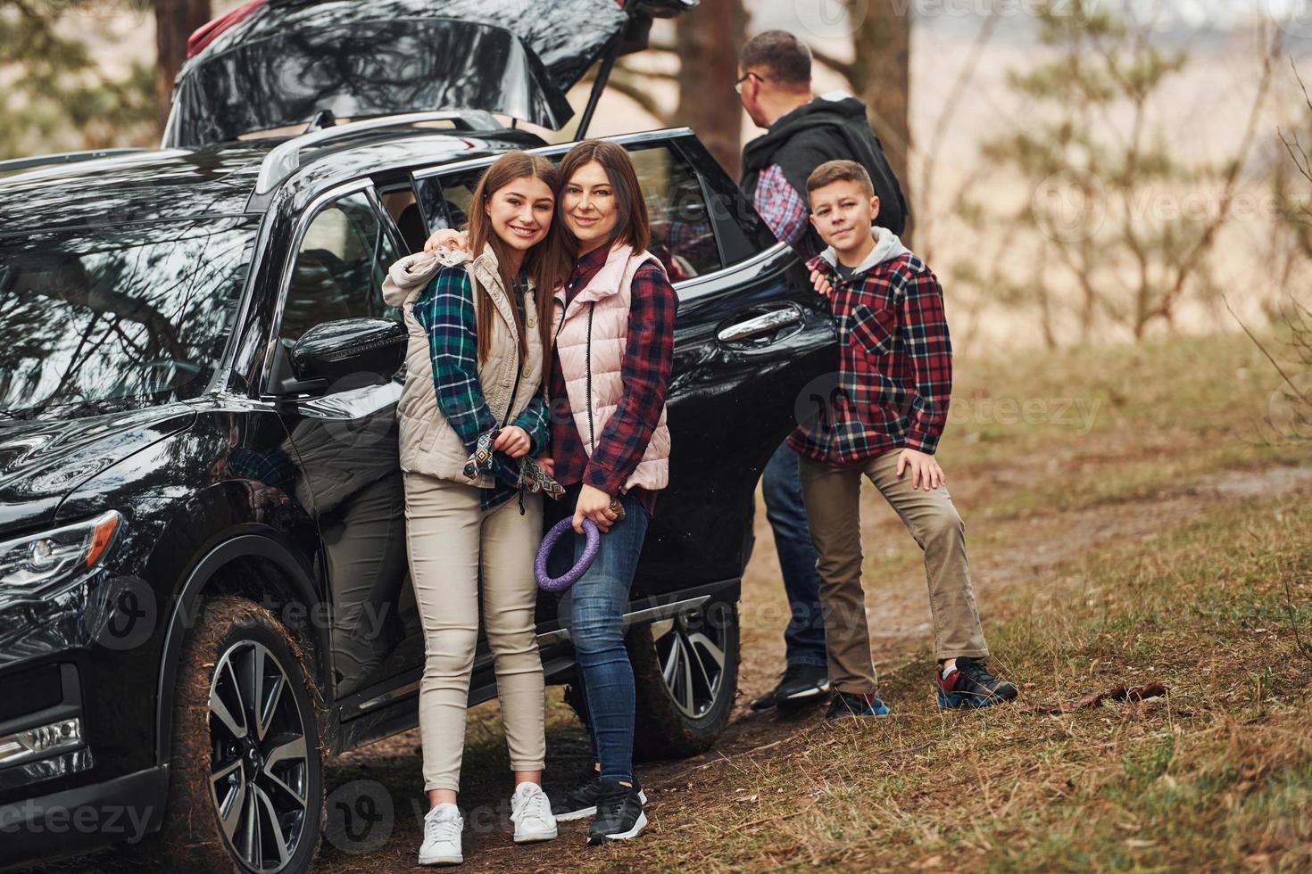 Happy family have fun with their dog near modern car outdoors in forest photo