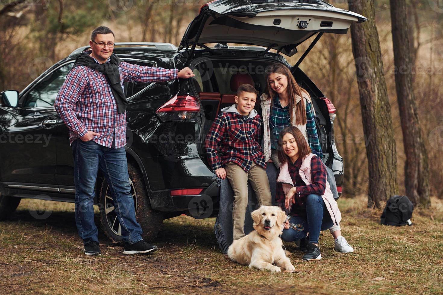 Happy family have fun with their dog near modern car outdoors in forest photo