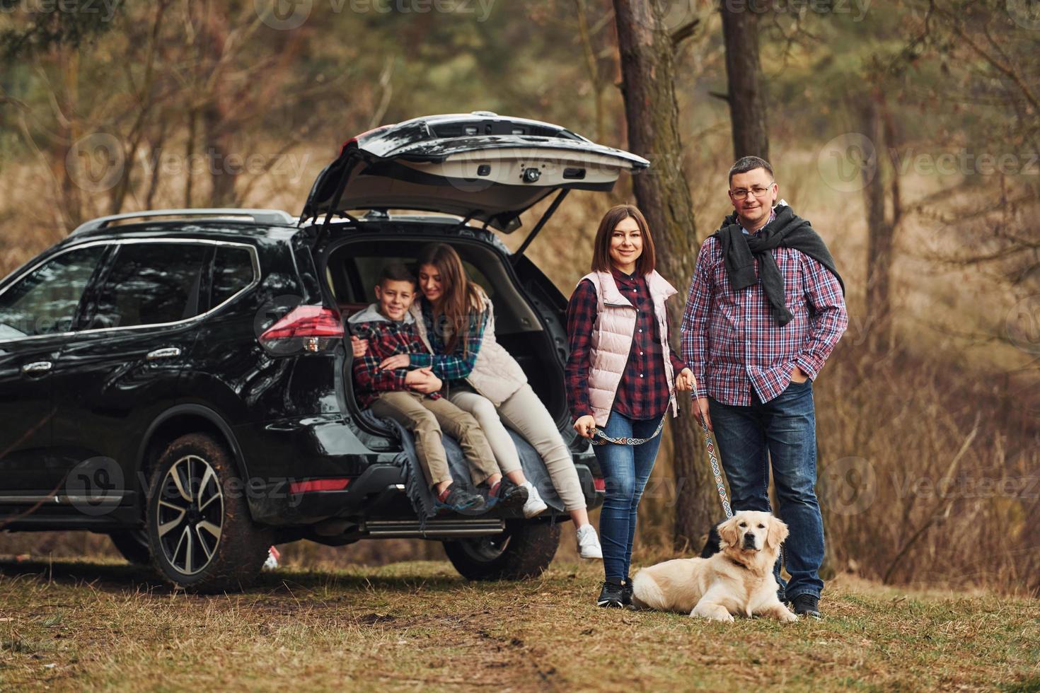 Happy family have fun with their dog near modern car outdoors in forest photo