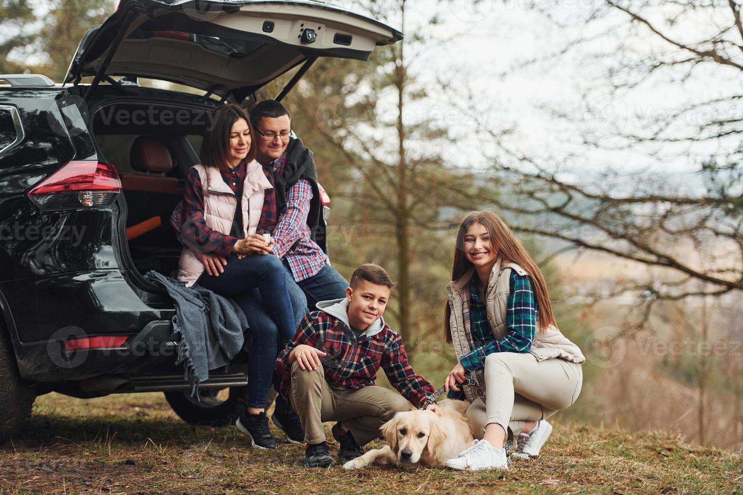 familia feliz sentada y divirtiéndose con su perro cerca de un camión moderno al aire libre en el bosque foto