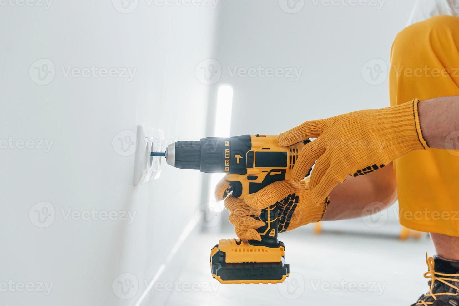 Handyman in yellow uniform works with electricity and installing new socket by using automatic screwdriver. House renovation conception photo
