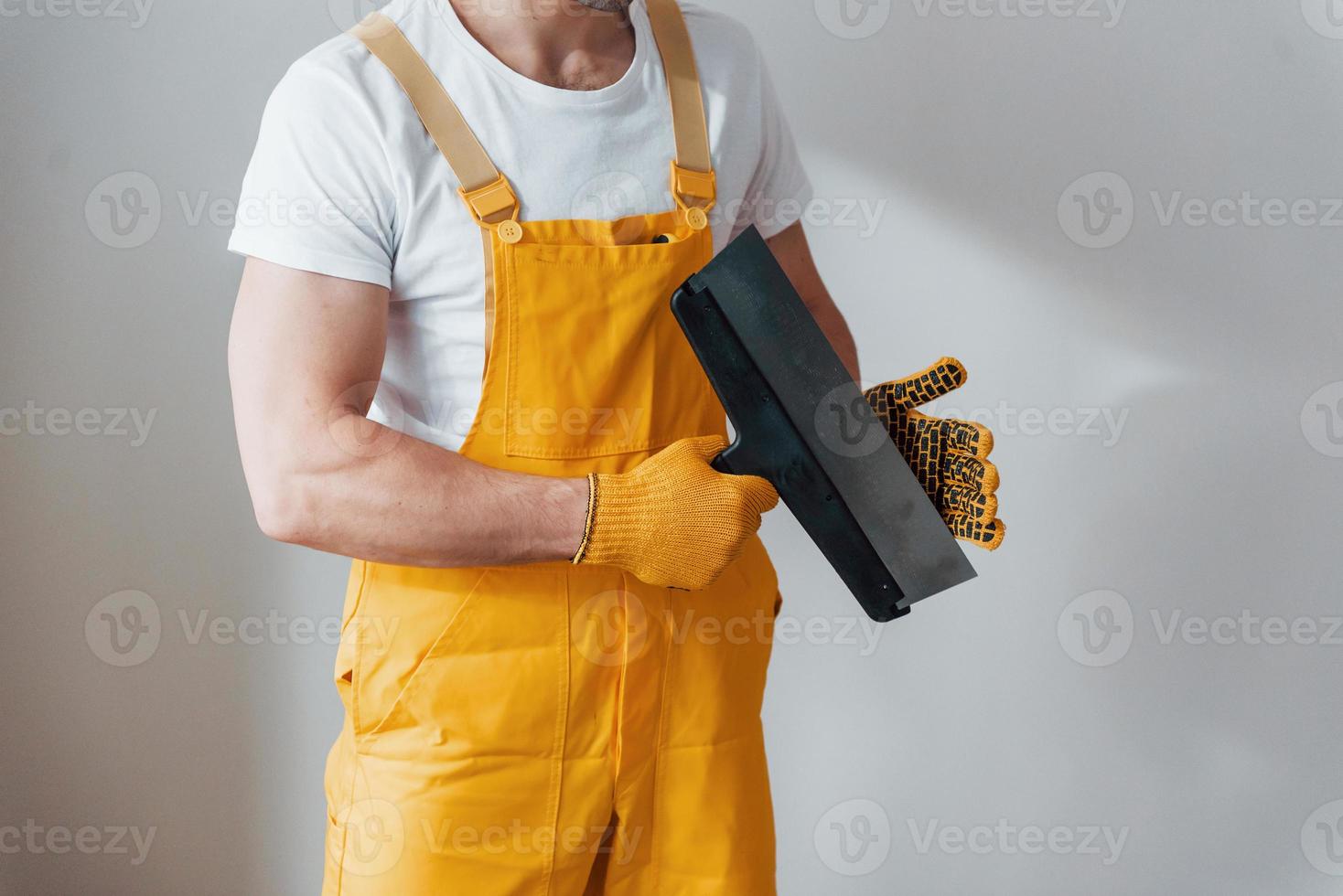 Handyman in yellow uniform standing against white wall. House renovation conception photo