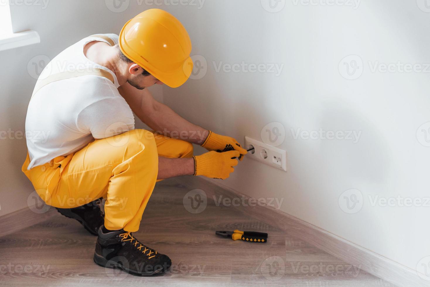 el manitas con uniforme amarillo trabaja con electricidad e instala un nuevo enchufe. concepción de renovación de la casa foto