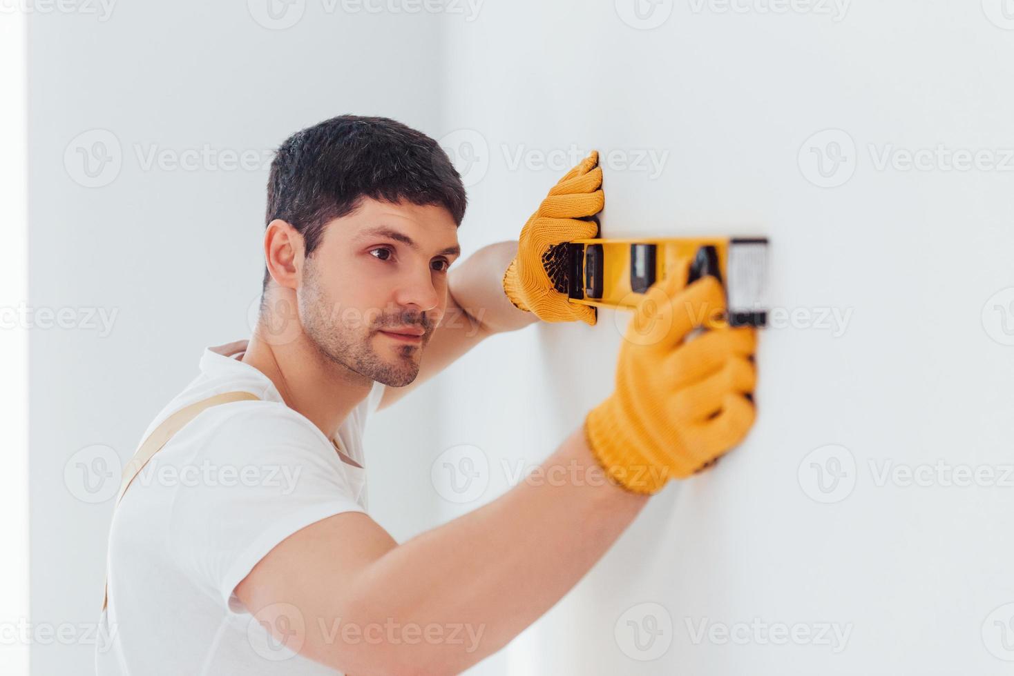 Handyman in yellow uniform checks levels of wall. House renovation conception photo