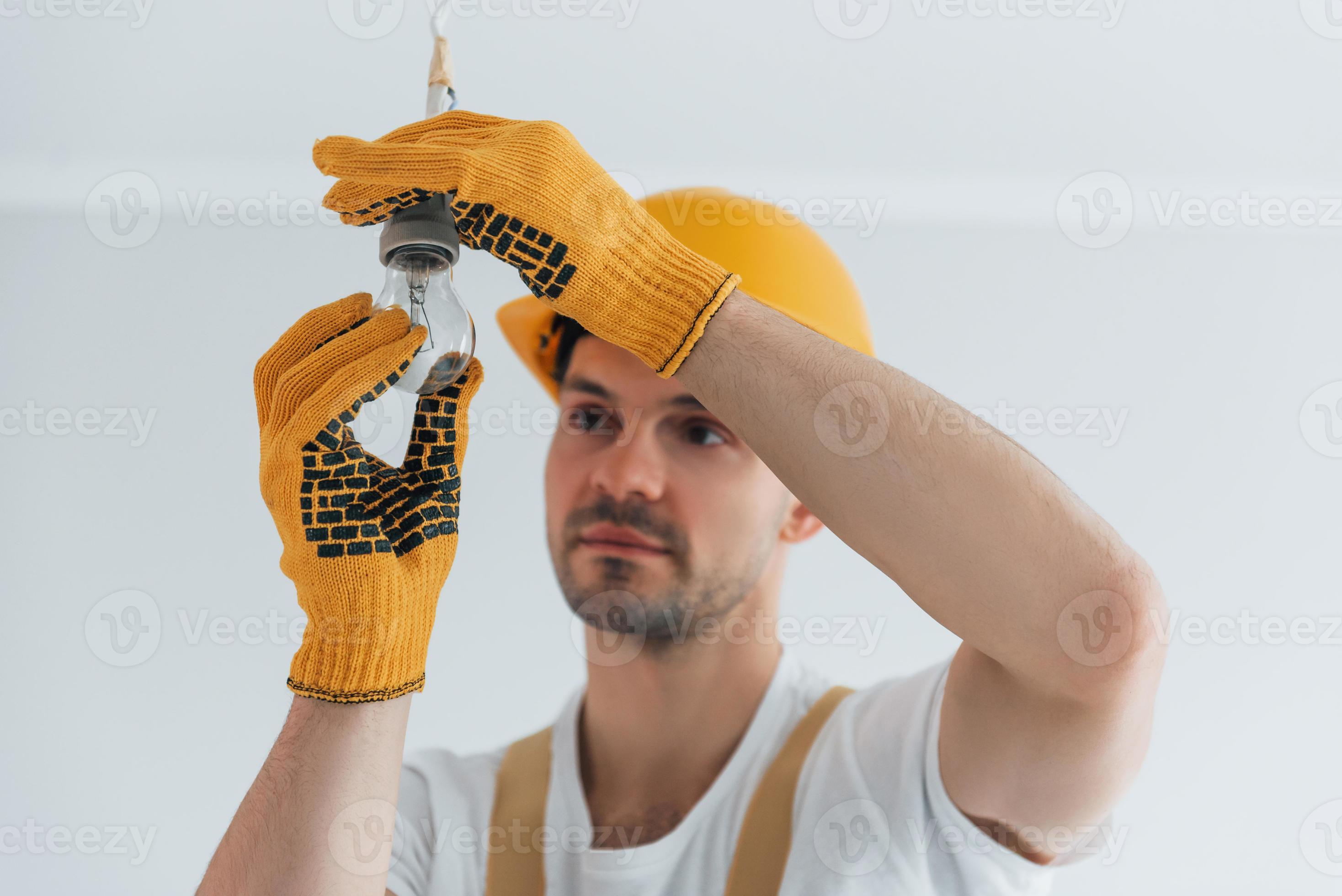 Handyman in yellow uniform changing light bulb. House renovation
