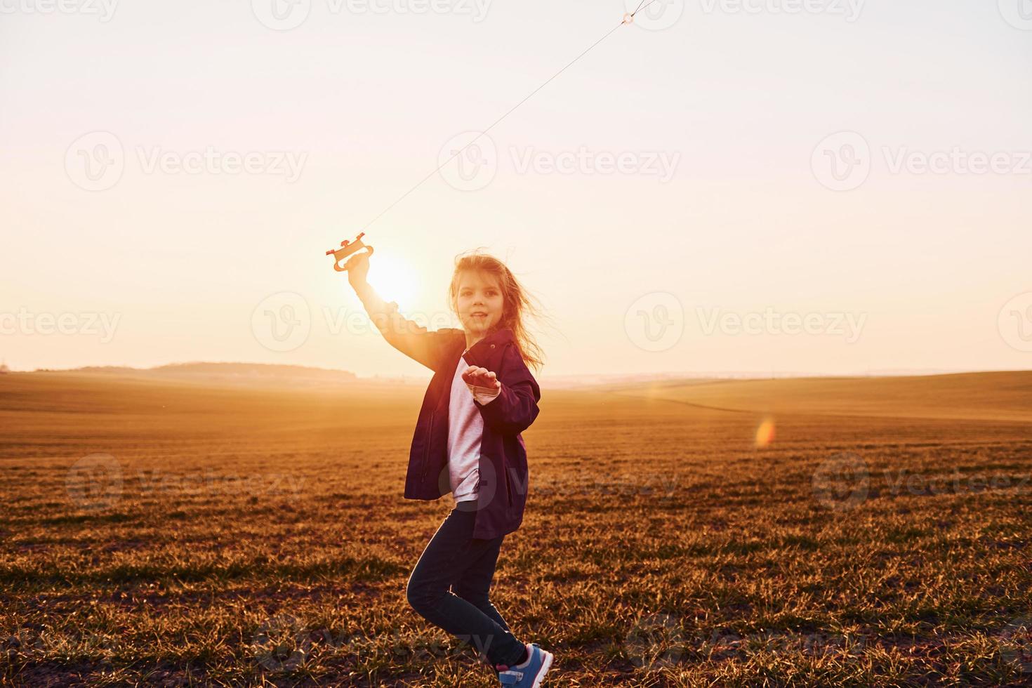 Happy little girl running with kite in hands on the beautiful field at sunrishe time photo