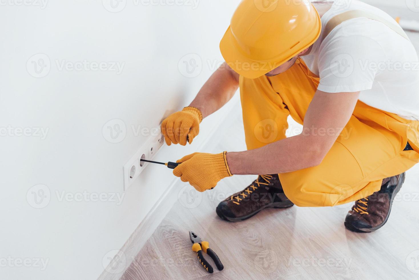 Handyman in yellow uniform works with electricity and installing new socket. House renovation conception photo