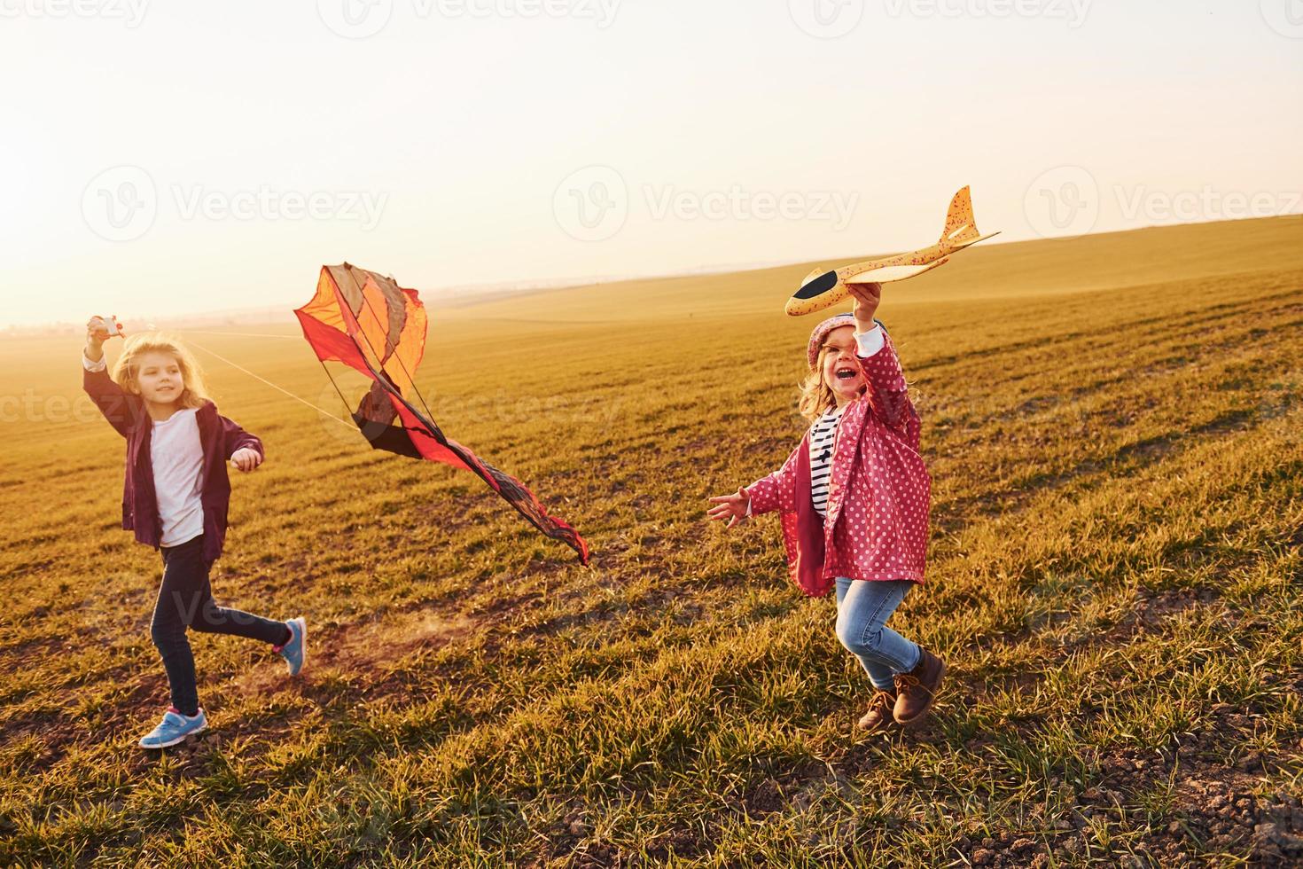 Two little girls friends have fun together with kite and toy plane on the field at sunny daytime photo