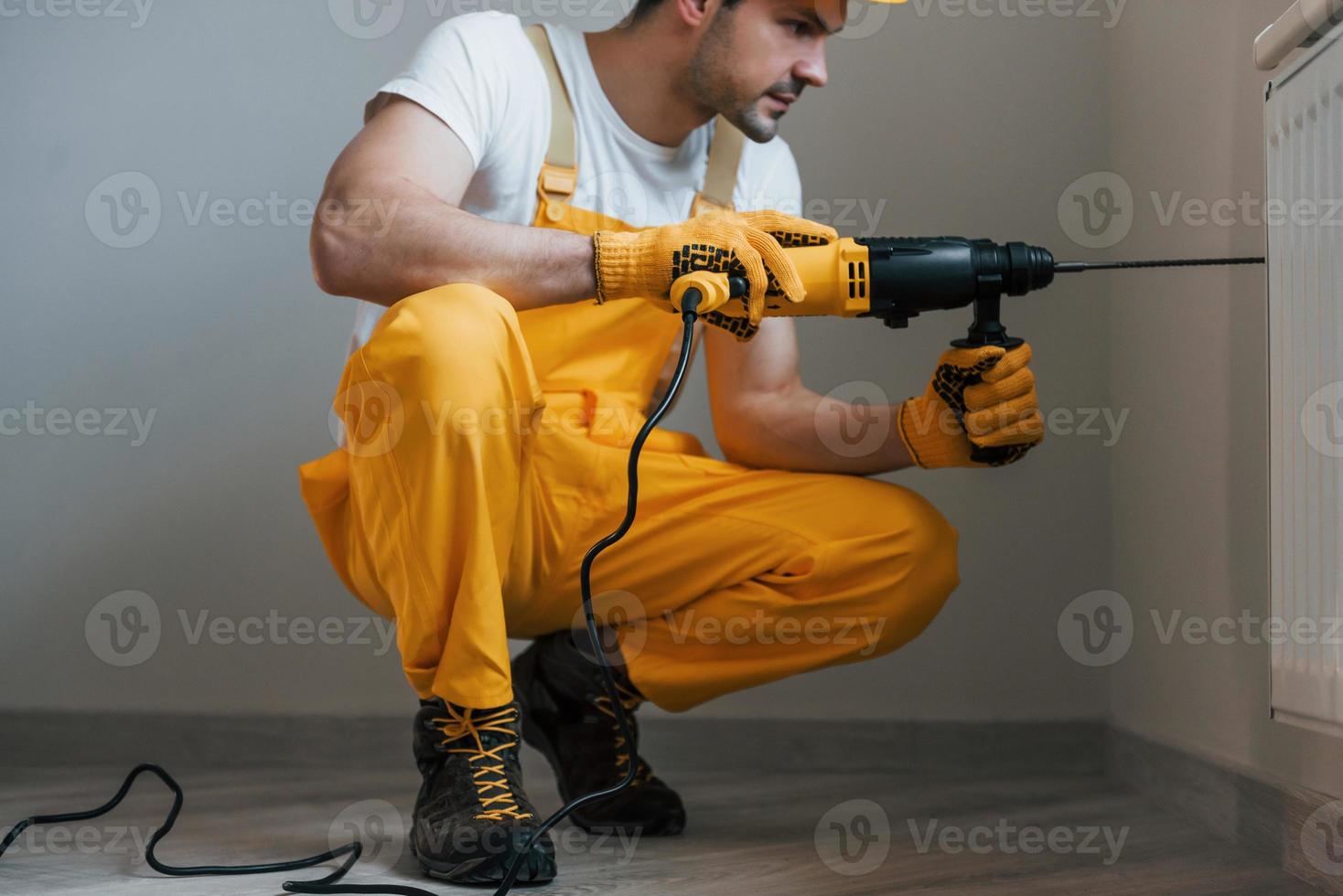 Handyman in yellow uniform works with drill indoors. House renovation conception photo