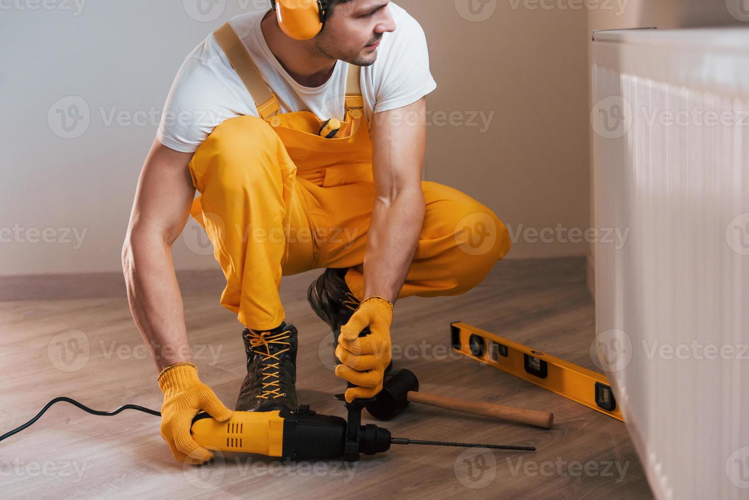 Handyman in yellow uniform works indoors by using hammer drill. House renovation conception photo