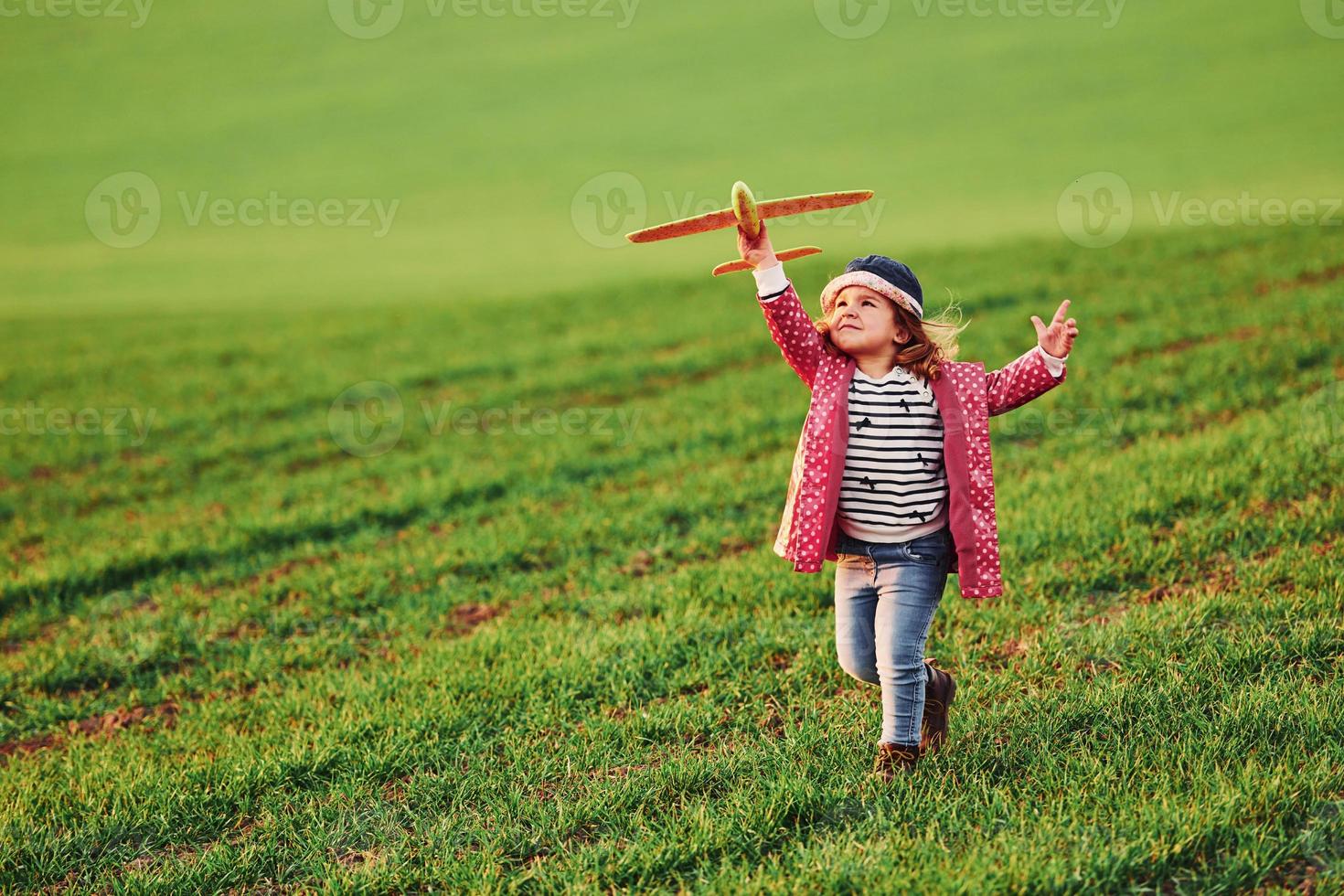 Cute little girl have fun with toy plane on the beautiful green field at sunny daytime photo