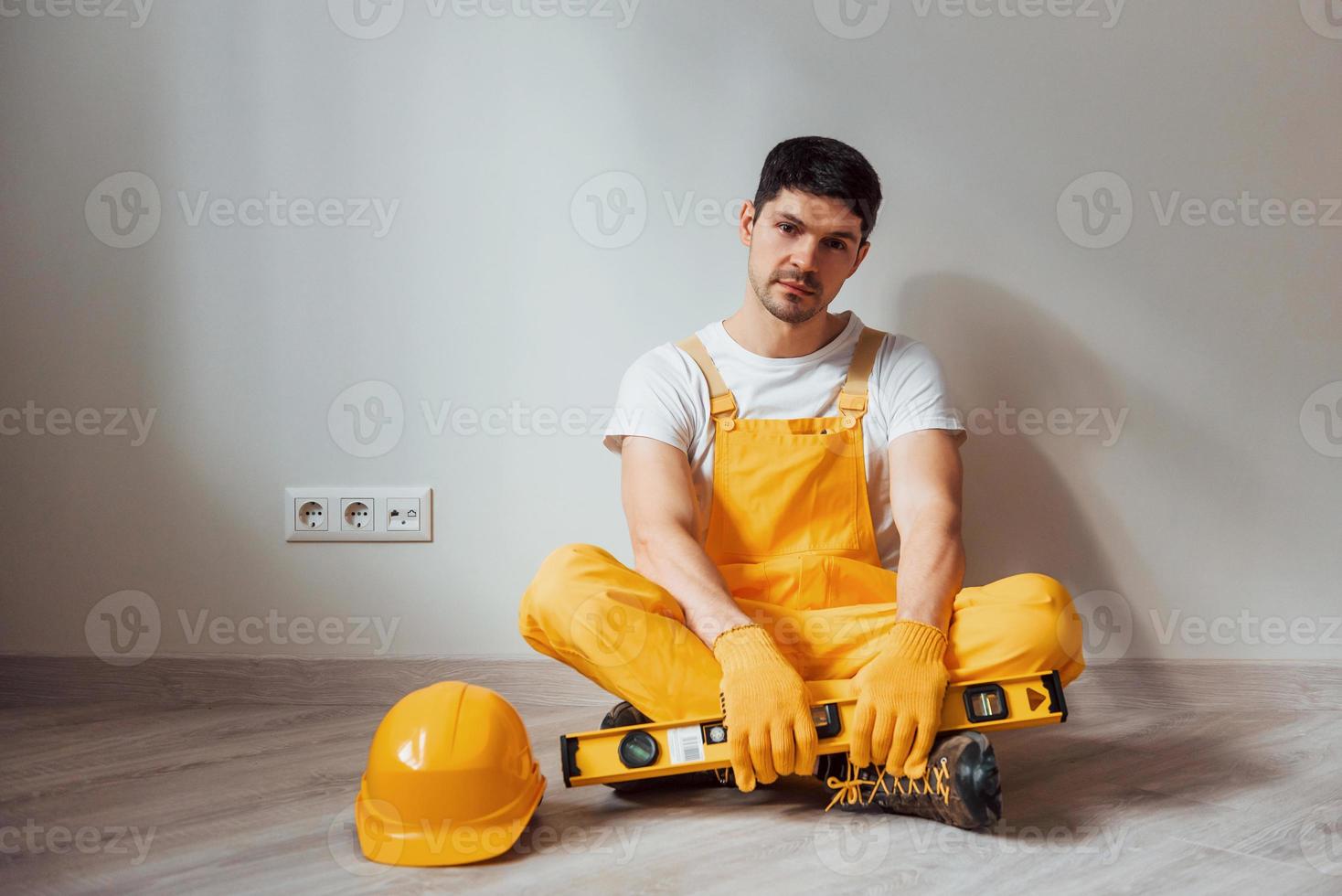 el manitas cansado con uniforme amarillo se sienta en el interior y toma un descanso. concepción de renovación de la casa foto