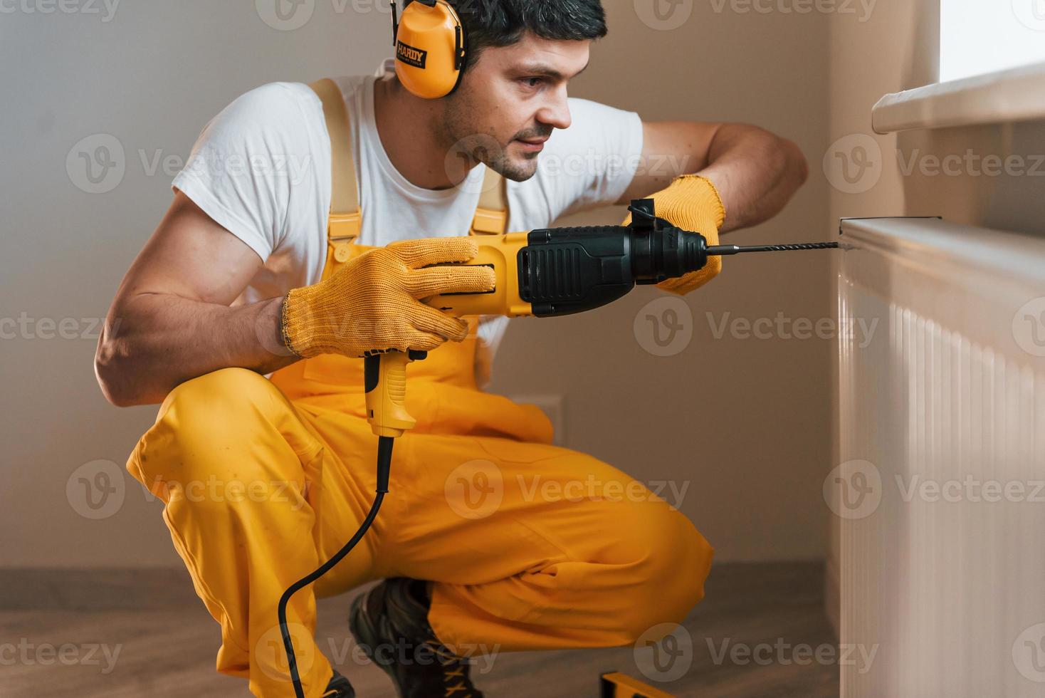 Handyman in yellow uniform works indoors by using hammer drill. House renovation conception photo