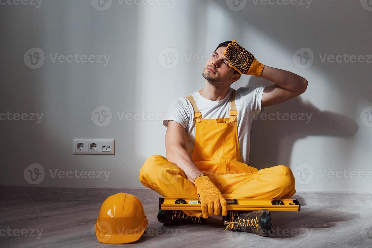 Tired handyman in yellow uniform sits indoors and takes break. House renovation conception photo