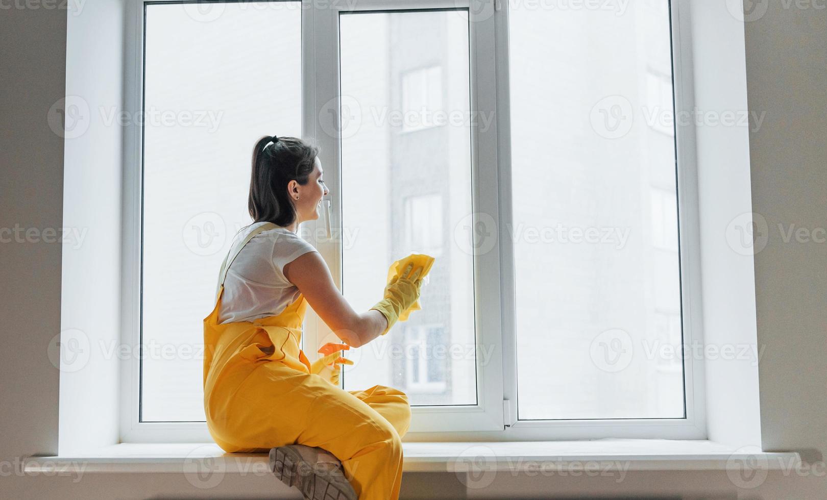 ama de casa con uniforme amarillo limpiando ventanas. concepción de renovación de la casa foto