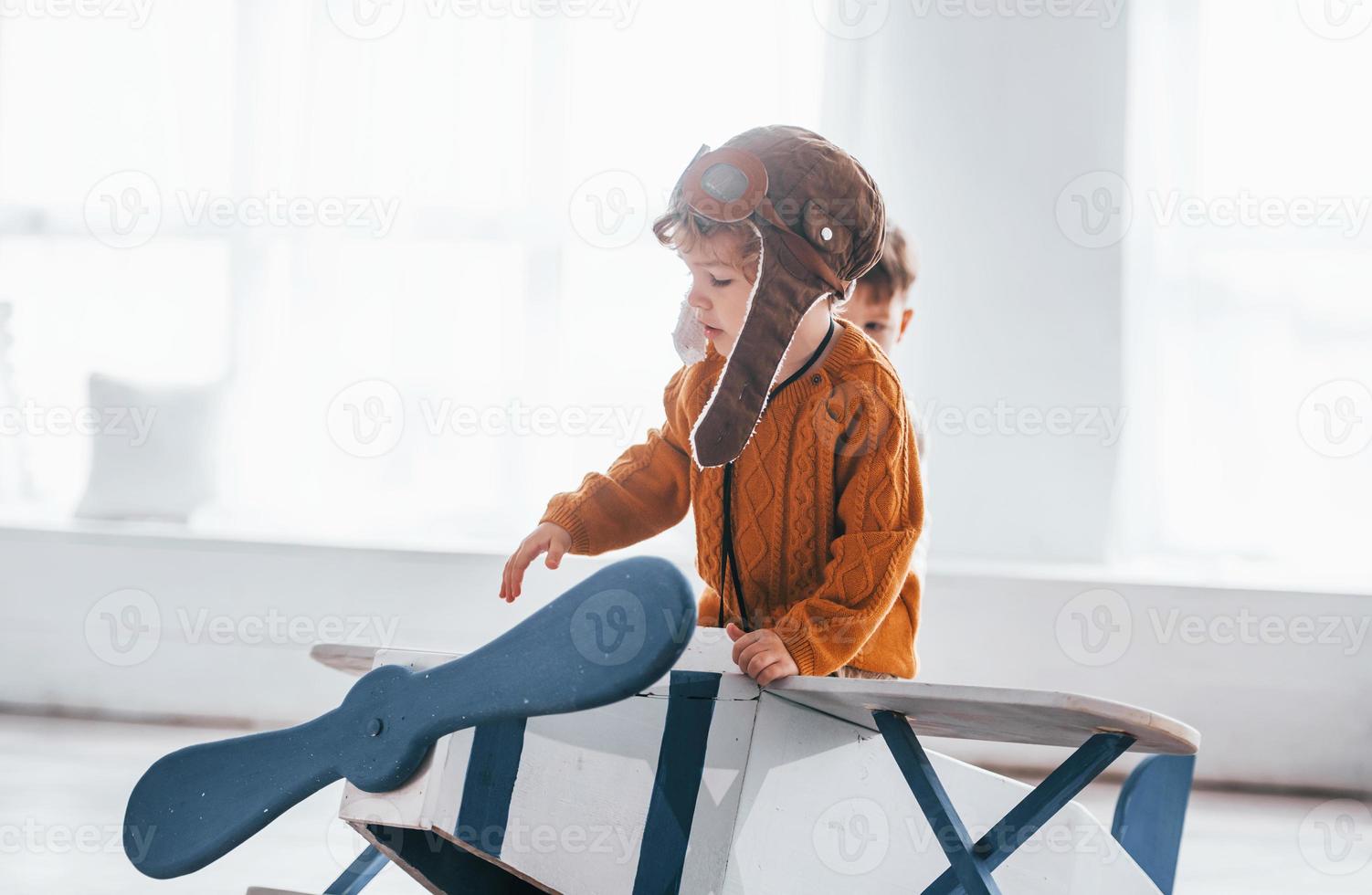 Little boy in retro pilot uniform having fun with toy plane indoors photo