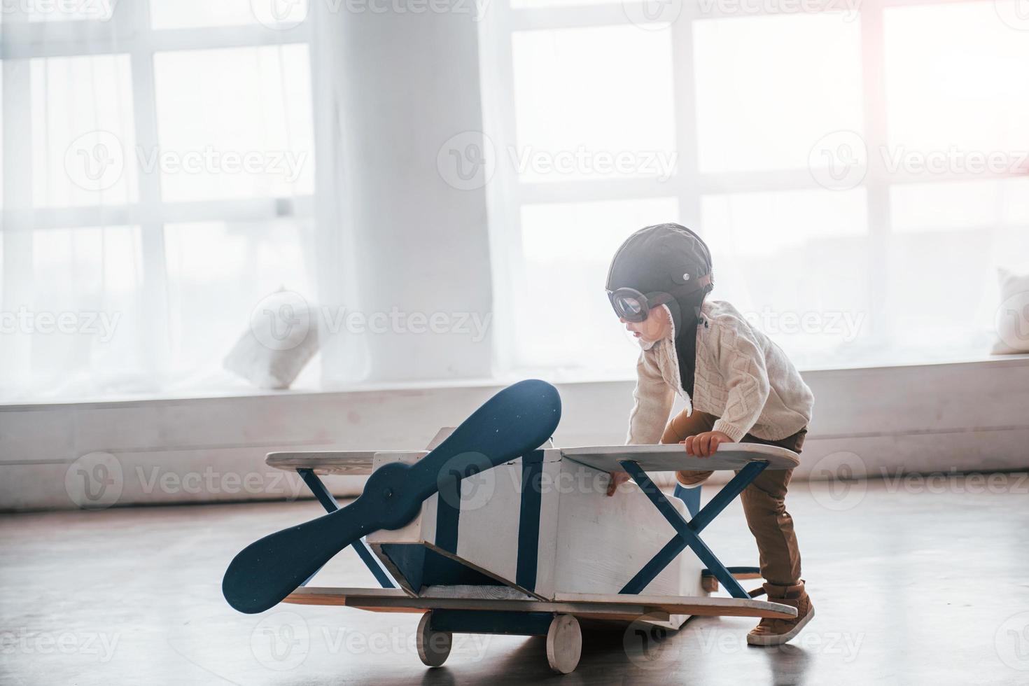 Little boy in retro pilot uniform having fun with toy plane indoors photo