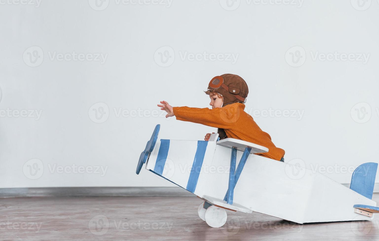 Little boy in retro pilot uniform having fun with toy plane indoors photo