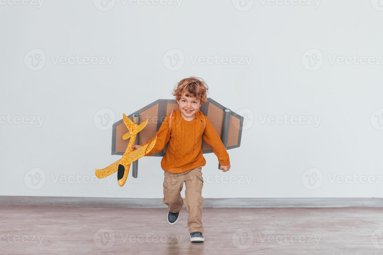 niño pequeño con uniforme de piloto retro corriendo con un avión de juguete en el interior foto