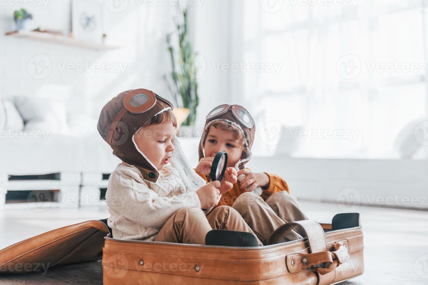 Two little boys have fun and sitting in suitcase indoors at daytime photo