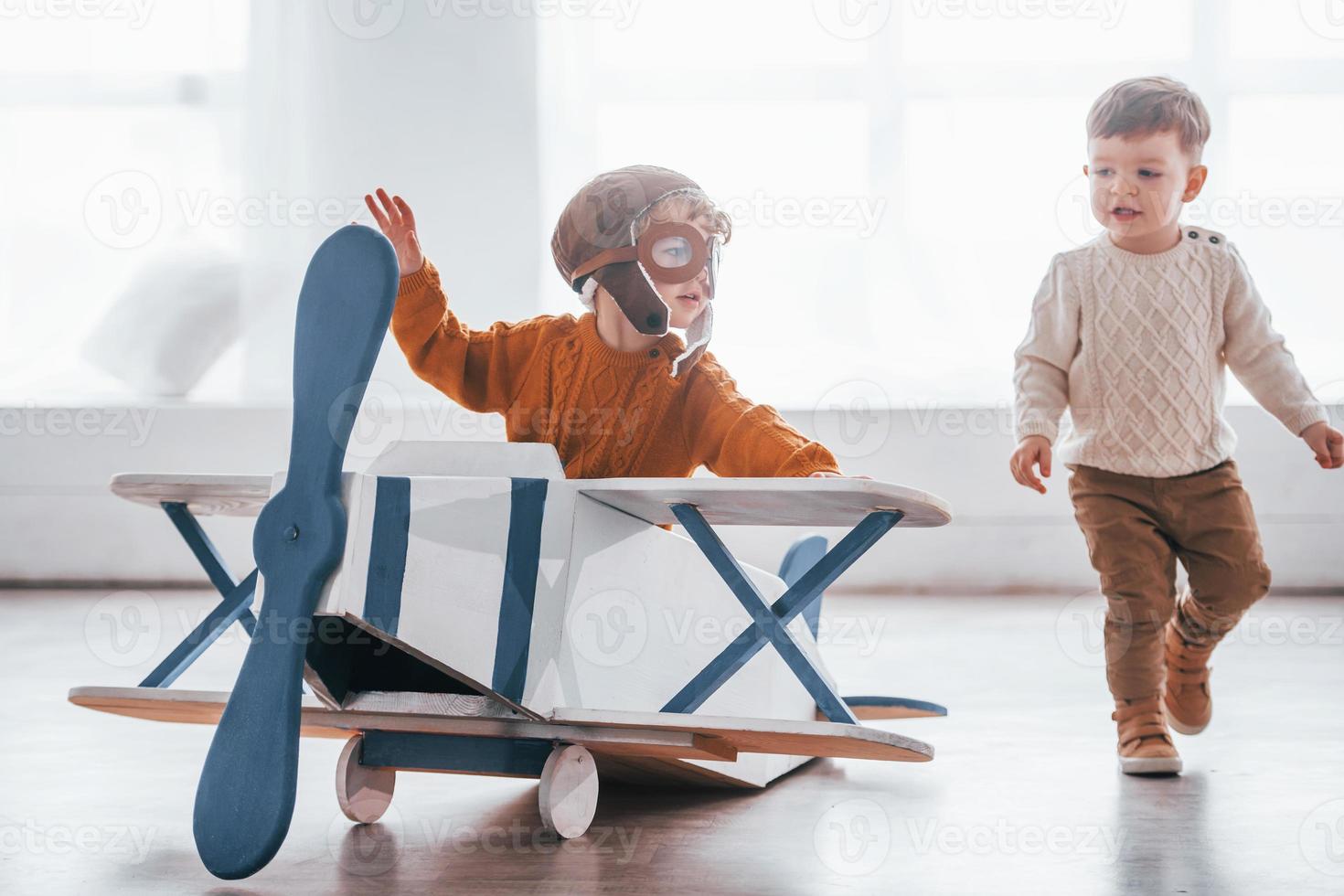 Two little boys in retro pilot uniform having fun with toy plane indoors photo