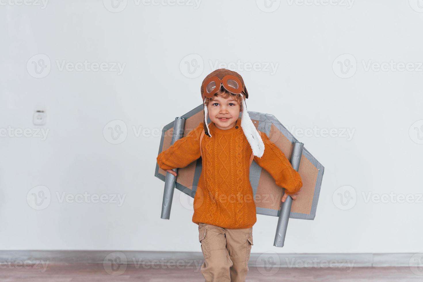 Little boy in retro pilot uniform running with toy plane indoors photo