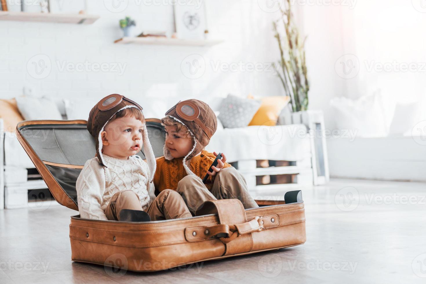 Two little boys have fun and sitting in suitcase indoors at daytime photo