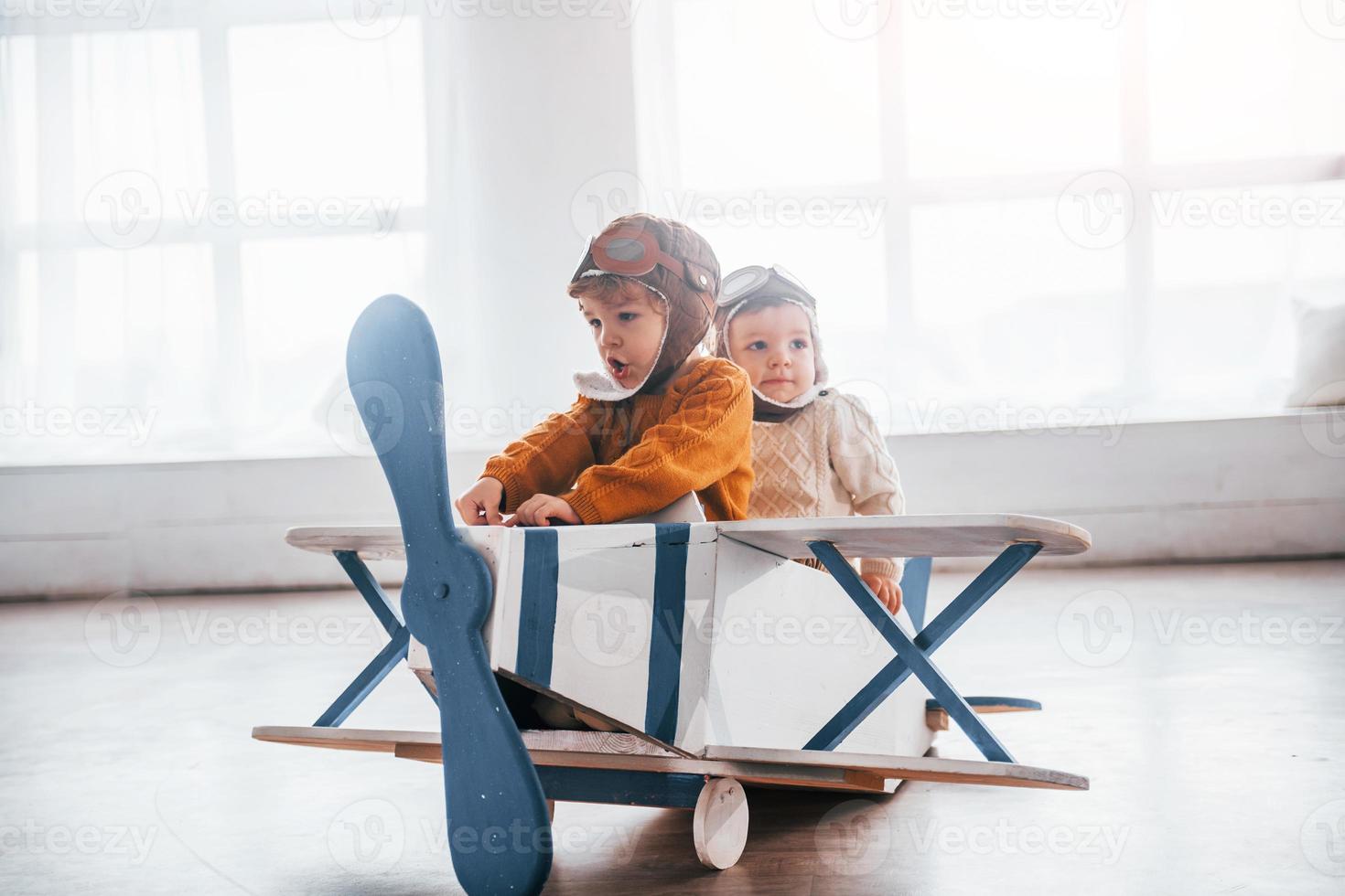 Two little boys in retro pilot uniform having fun with toy plane indoors photo