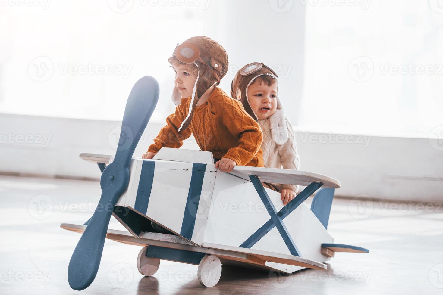 Two little boys in retro pilot uniform having fun with toy plane indoors photo