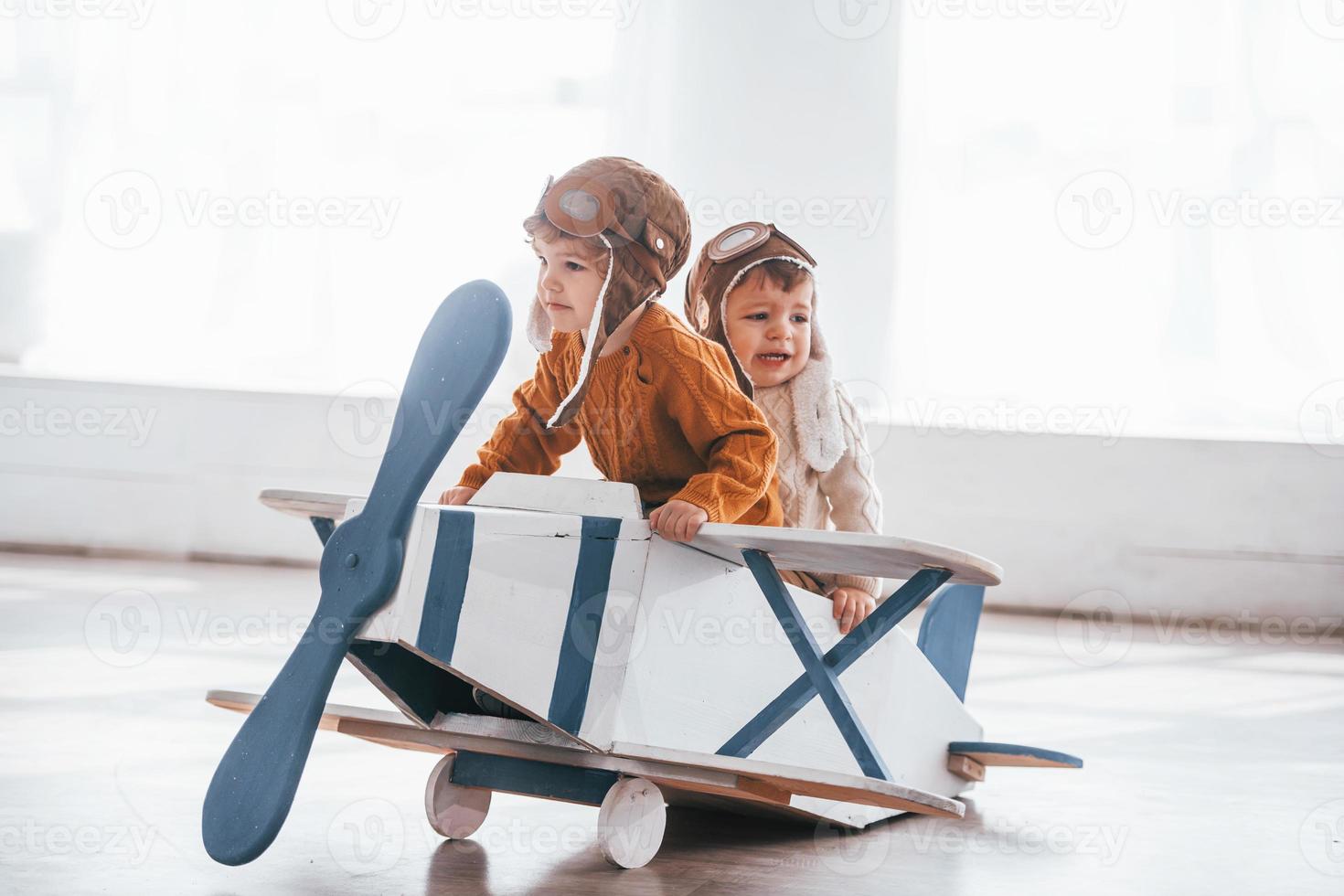 Two little boys in retro pilot uniform having fun with toy plane indoors photo