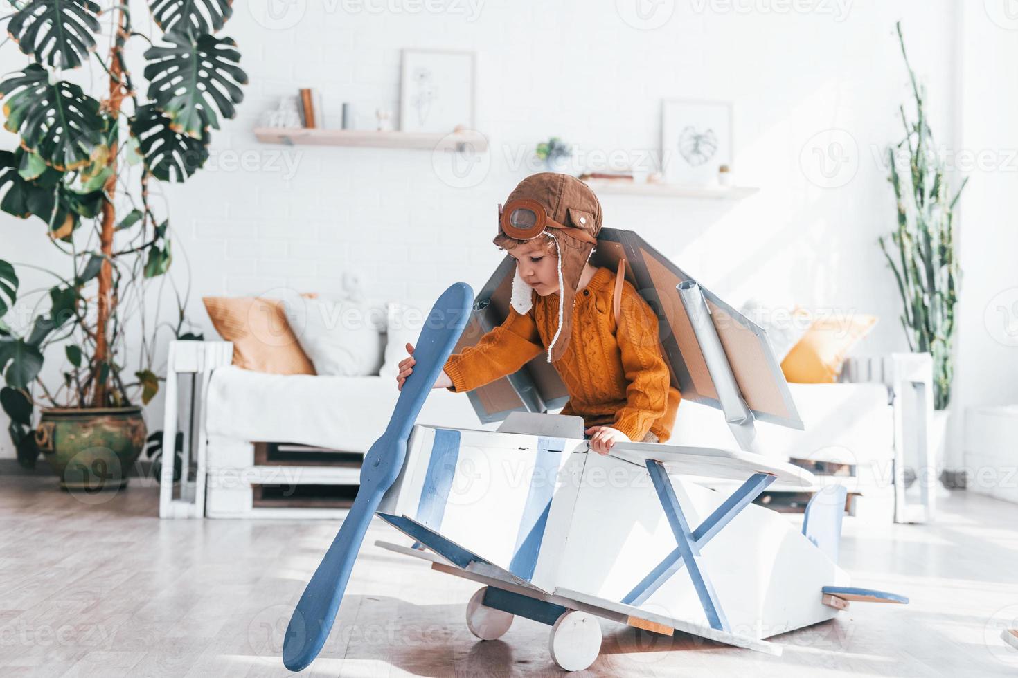 Little boy in retro pilot uniform having fun with toy plane indoors photo