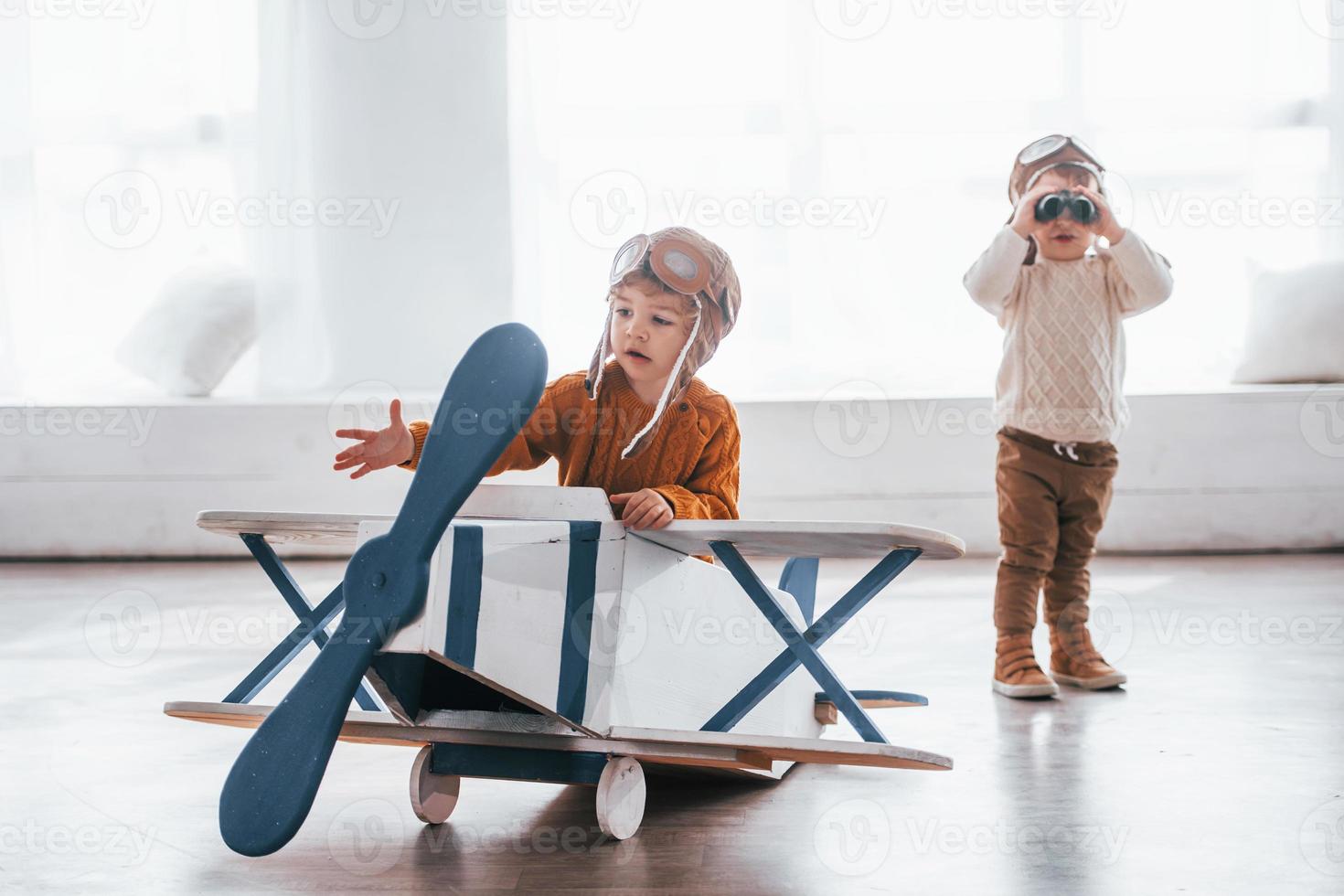 Two little boys in retro pilot uniform having fun with toy plane indoors photo